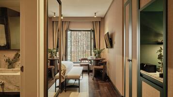 A hotel room with a large window, a sofa, a dining table with chairs, and a mirror on the wall.