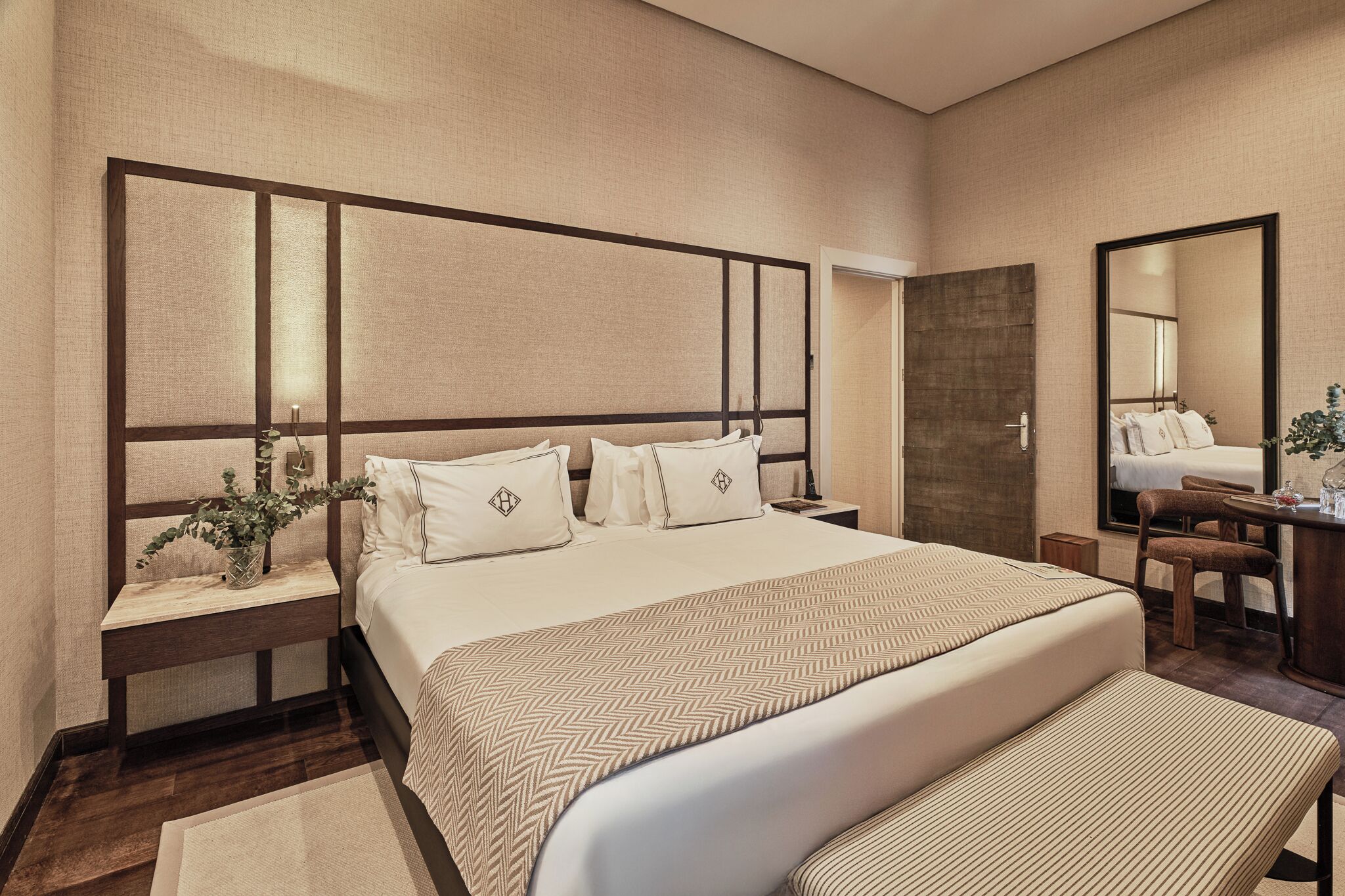 A hotel room with a large bed, bedside tables, a desk, a chair, and a mirror.