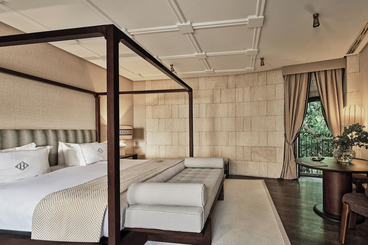 A bedroom with a four-poster bed, a sofa, and a small table with a plant.