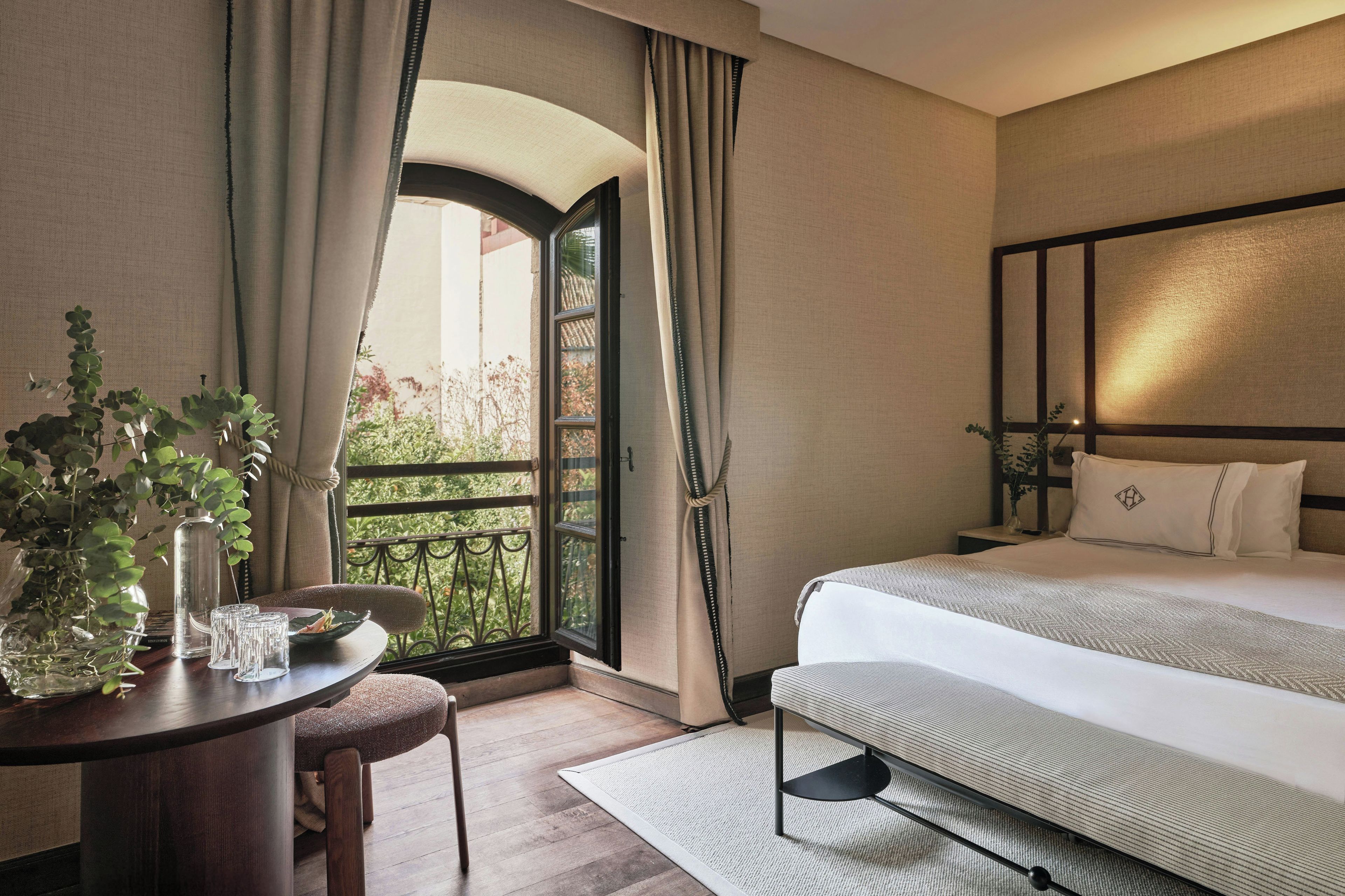 Une chambre d’hôtel avec un lit, un bureau et une chaise, une fenêtre avec des rideaux et une vue sur la verdure.