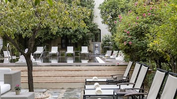 Un área junto a la piscina con sillones de descanso, un camino de piedra y abundante vegetación.