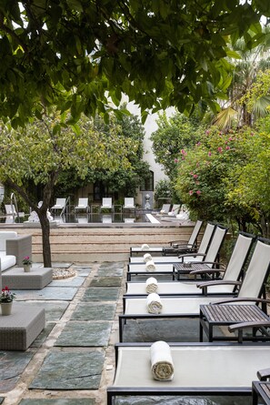 Un espace aménagé au bord de la piscine, avec des chaises longues, un chemin en pierre et une végétation luxuriante.