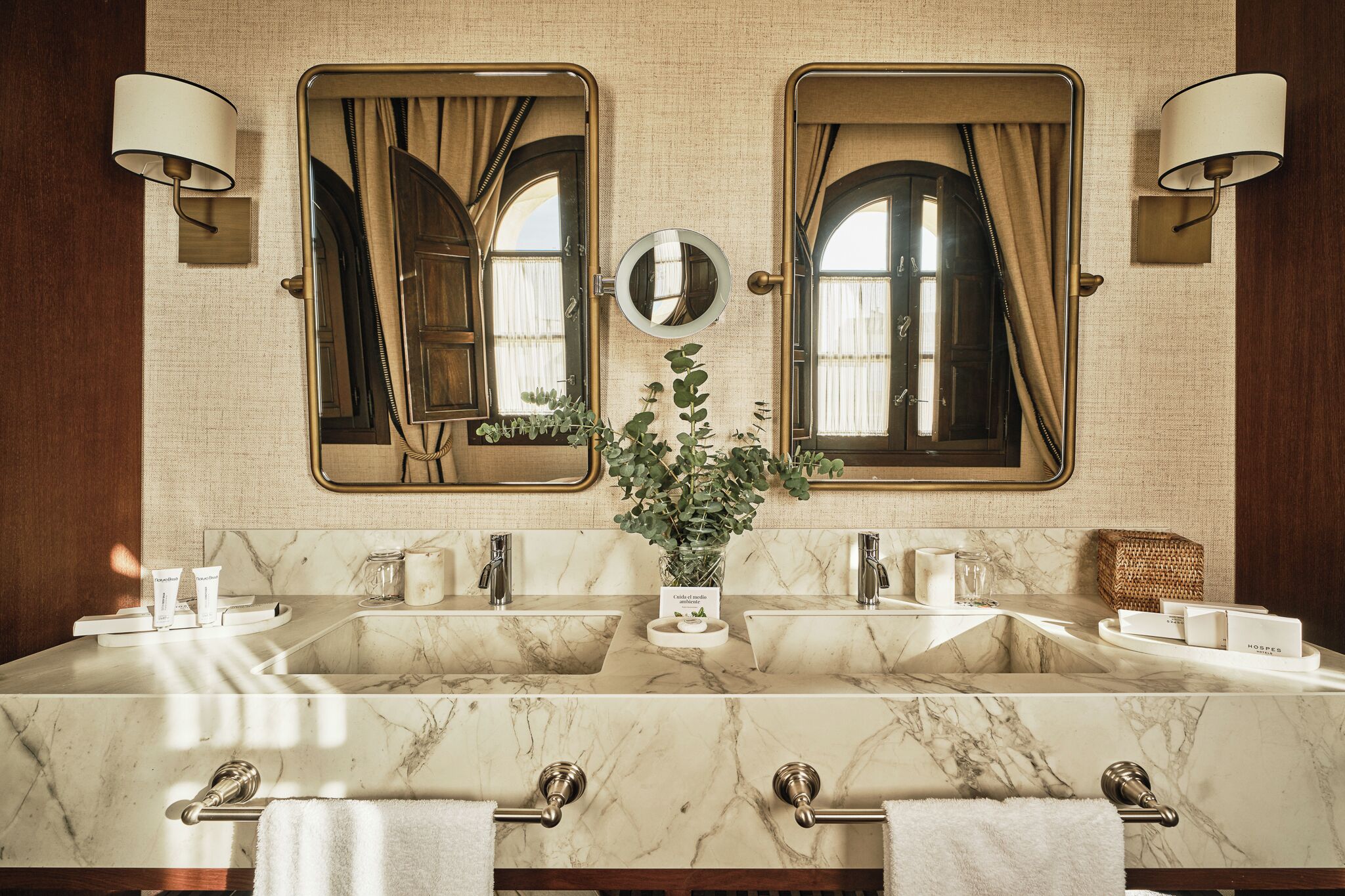 A bathroom with a large marble sink, two mirrors, and a potted plant.