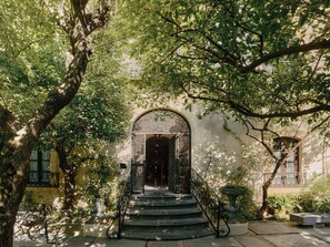 A building entrance with a staircase leading up to an arched doorway, surrounded by trees and greenery. - Hospes Palacio del Bailío, a Member of Design Hotels (Córdoba)