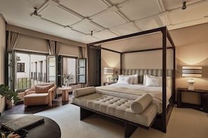 A spacious bedroom with a four-poster bed, a sitting area, and a view of the outdoors.