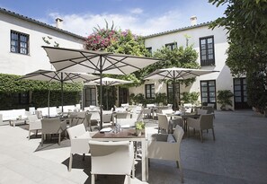 Een terras buiten met tafels, stoelen, parasols en potplanten.
