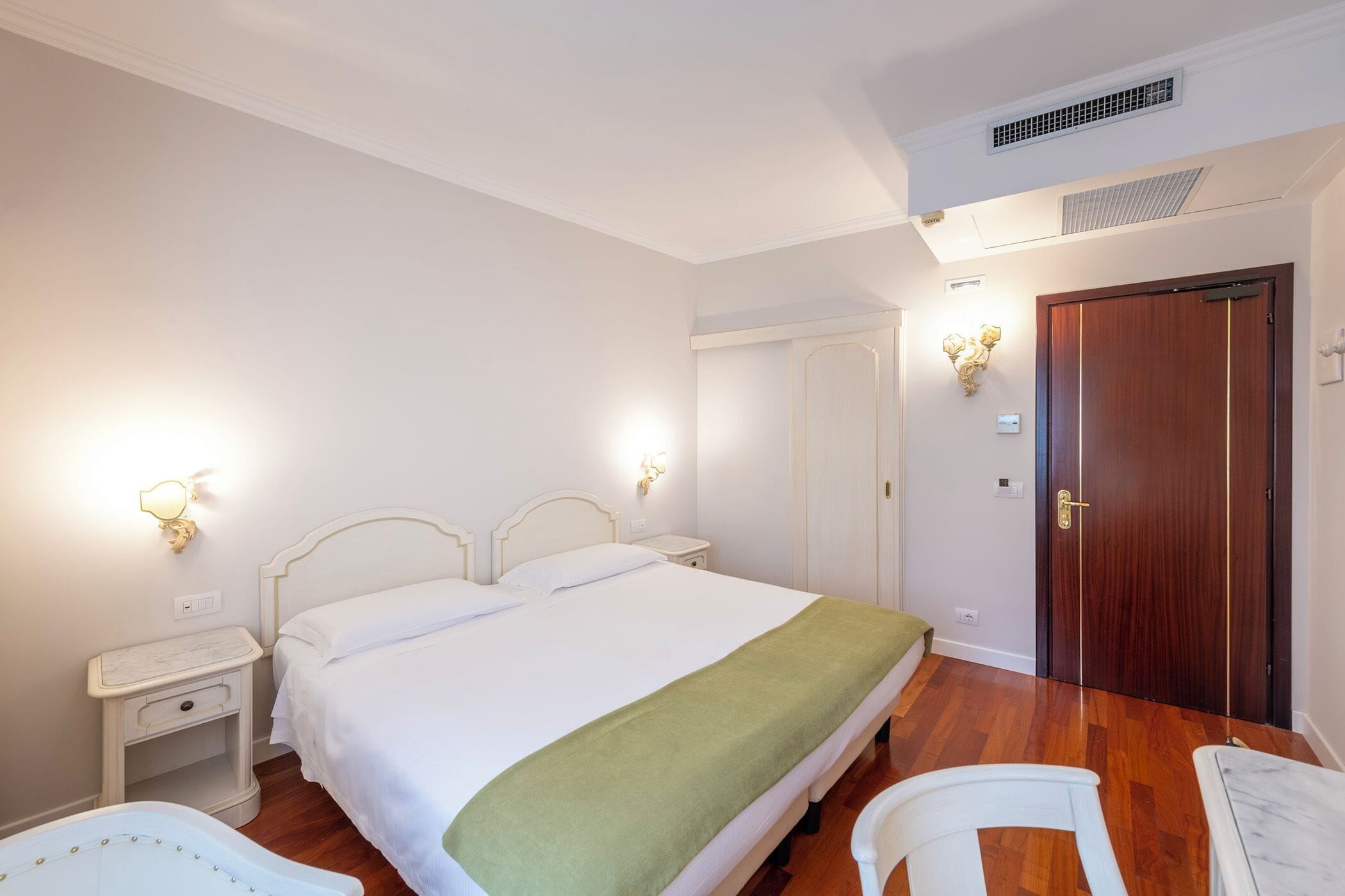Quarto com uma cama grande, mesas de cabeceira, um guarda-roupa e uma porta.