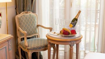 Une pièce avec un fauteuil ancien, une petite table sur laquelle se trouvent une bouteille de champagne, des verres et un saladier rempli de fruits.