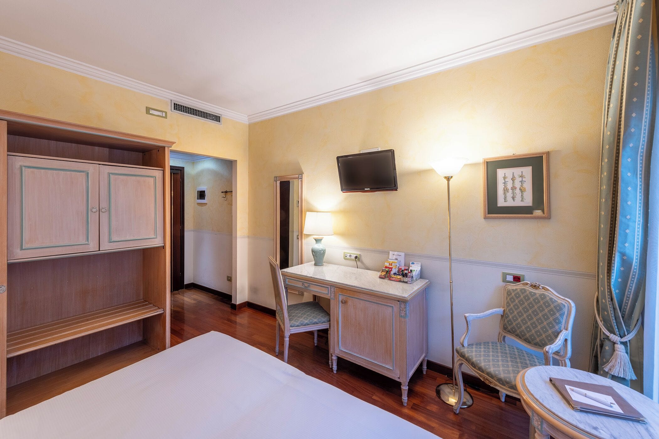 Ein Hotelzimmer mit einem Bett, einem Schreibtisch mit Stuhl, einem Fernseher und einem Fenster mit Vorhängen.