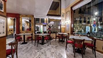 Un restaurant doté d’un sol en marbre, de chaises à coussins rouges et de tableaux encadrés qui ornent les murs.