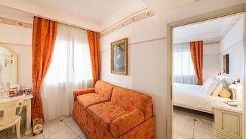 A hotel room with a sofa, a bed, a desk with a mirror, and a painting on the wall.