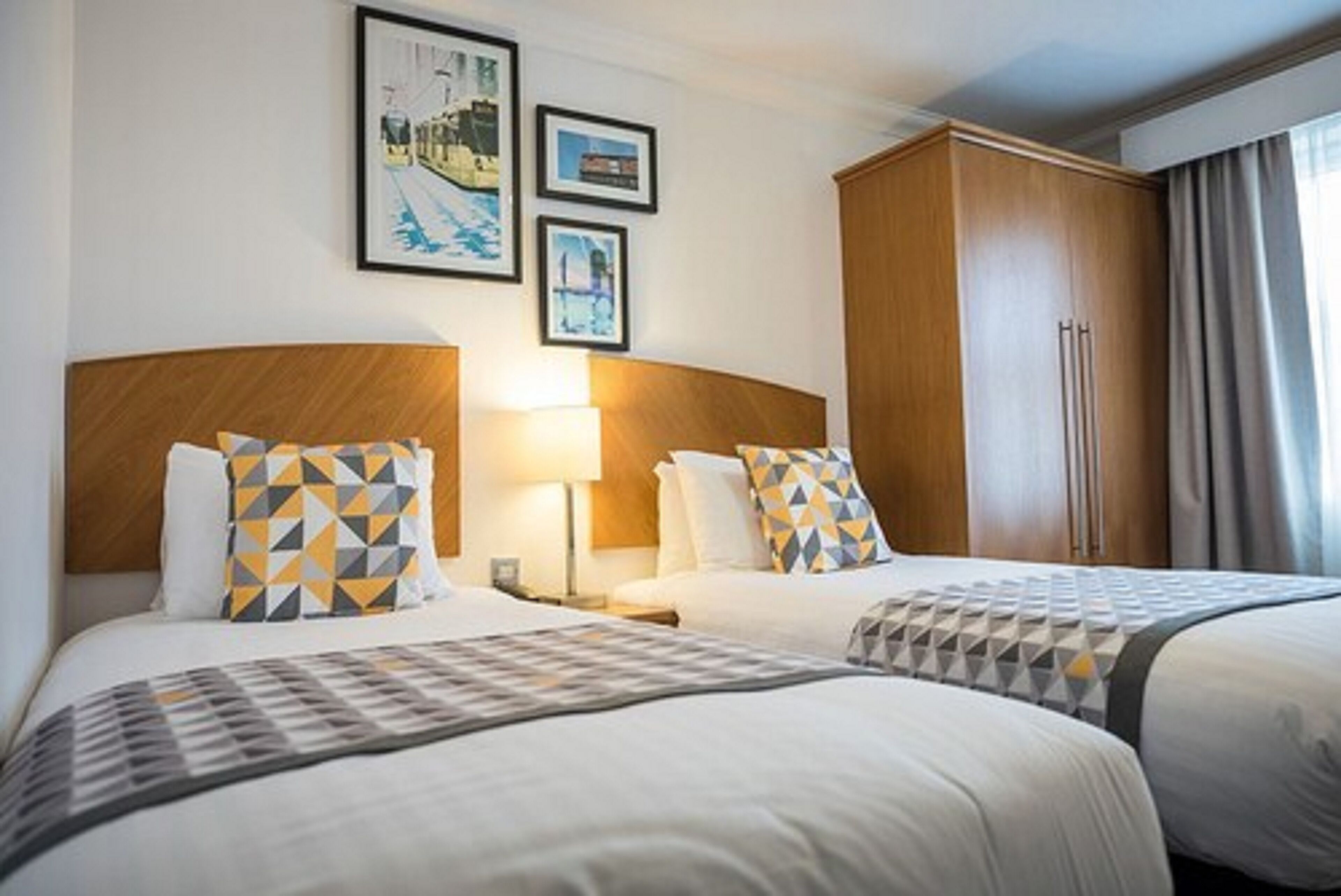 A hotel room with two beds, a wooden wardrobe, and framed pictures on the wall.