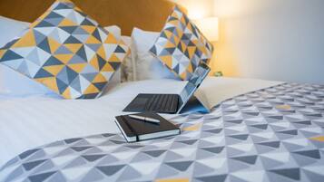 A bed with a laptop, a notebook, and a pen on a bed with a geometric patterned bedspread.