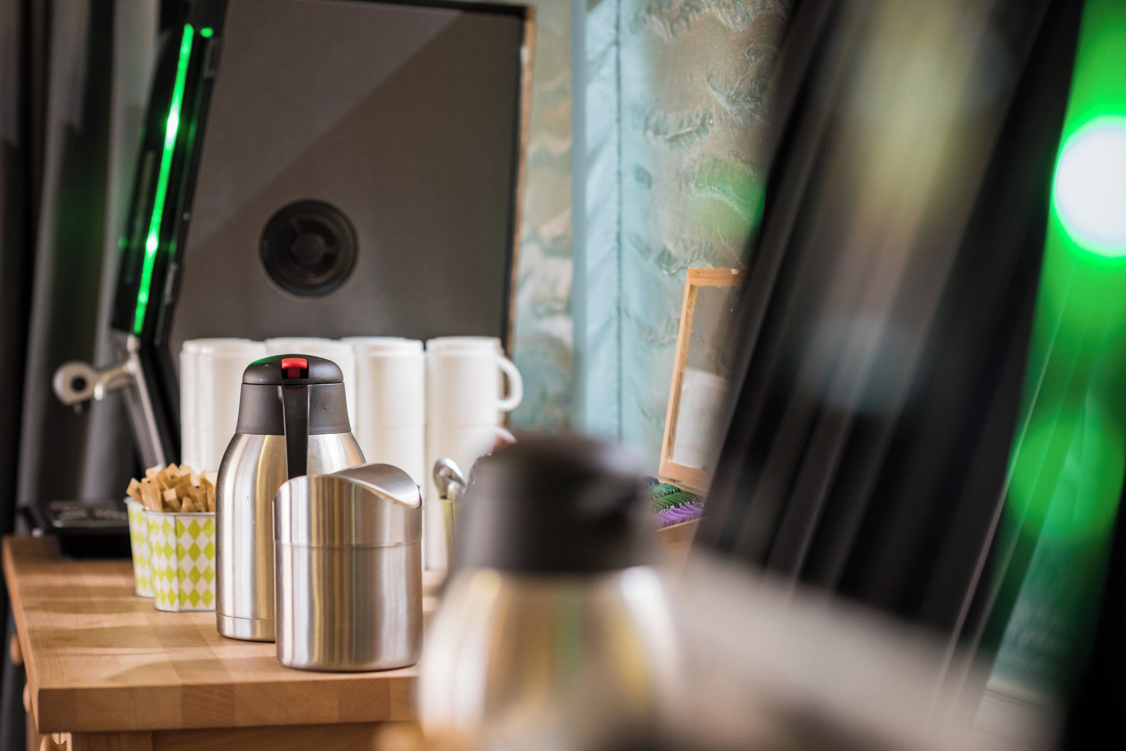 A kitchen counter with various appliances and items, including a coffee maker, a kettle, and a thermos.