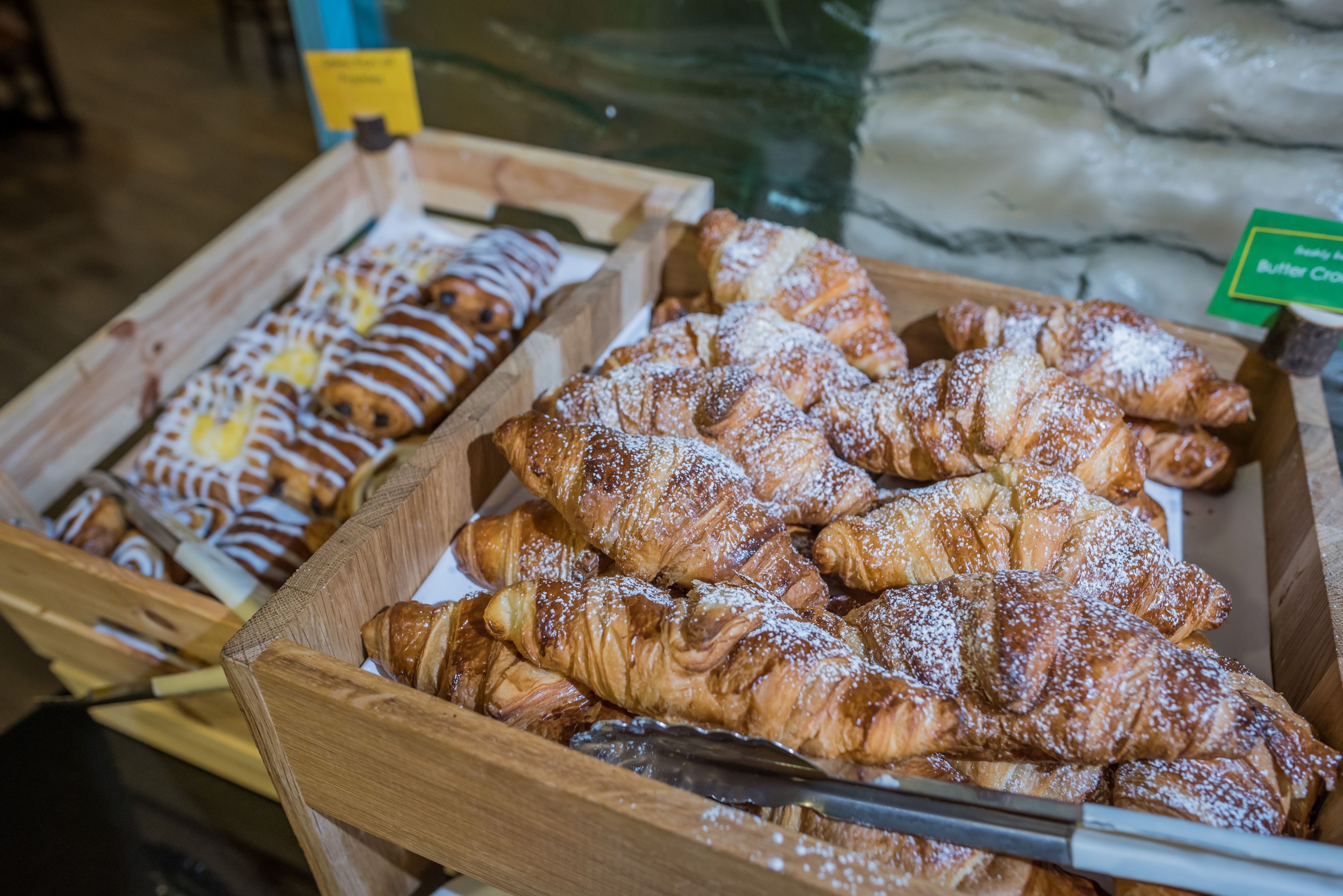 Une variété de pâtisseries présentées dans des boîtes en bois, notamment des croissants et d’autres produits de boulangerie.