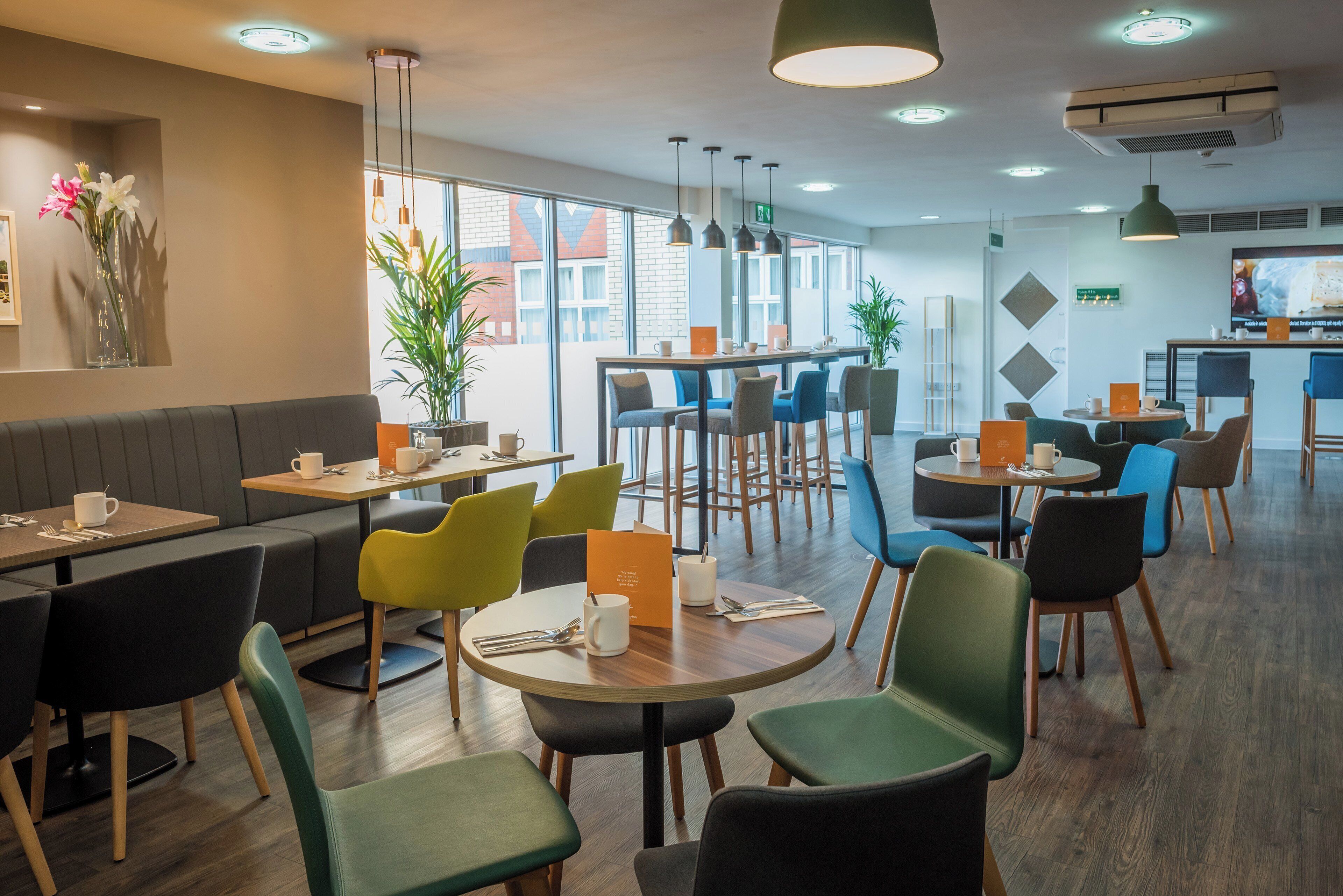 A modern cafe with round tables, colorful chairs, and a large window offering a view of the city.