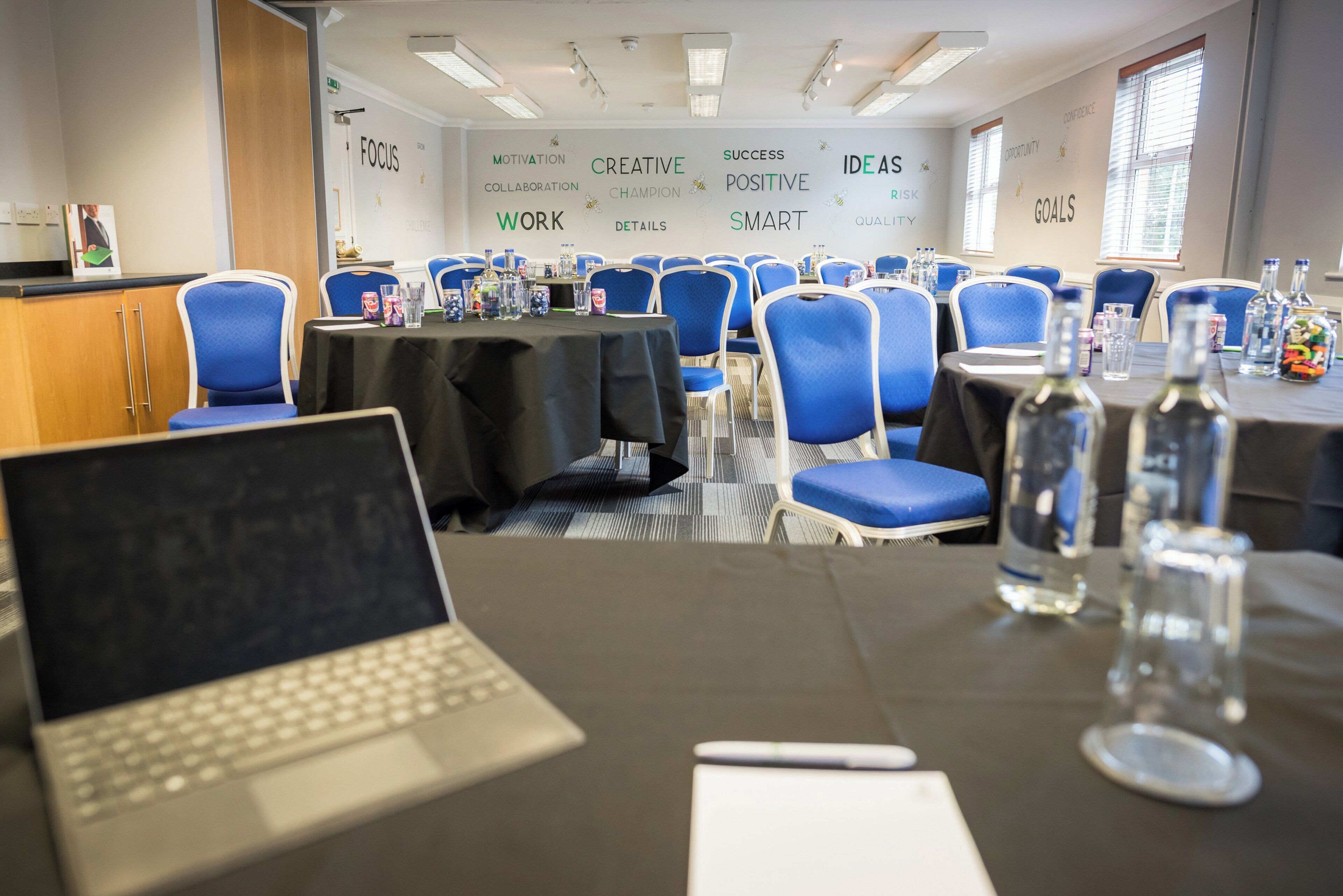 A conference room with round tables, blue chairs, and a laptop on one table.