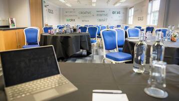 A conference room with round tables, blue chairs, and a laptop on one table.