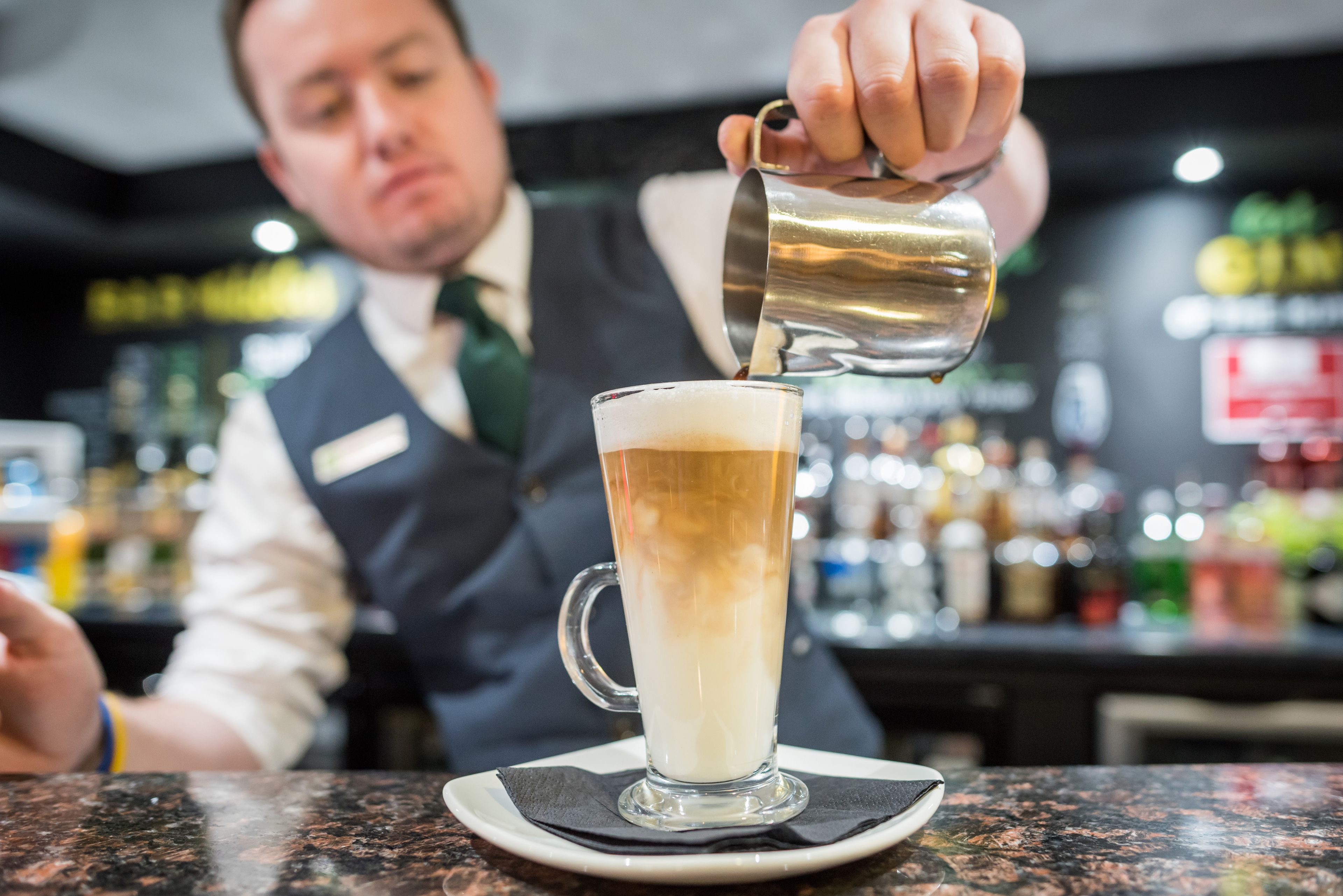 A barista pouring a beverage into a tall glass.