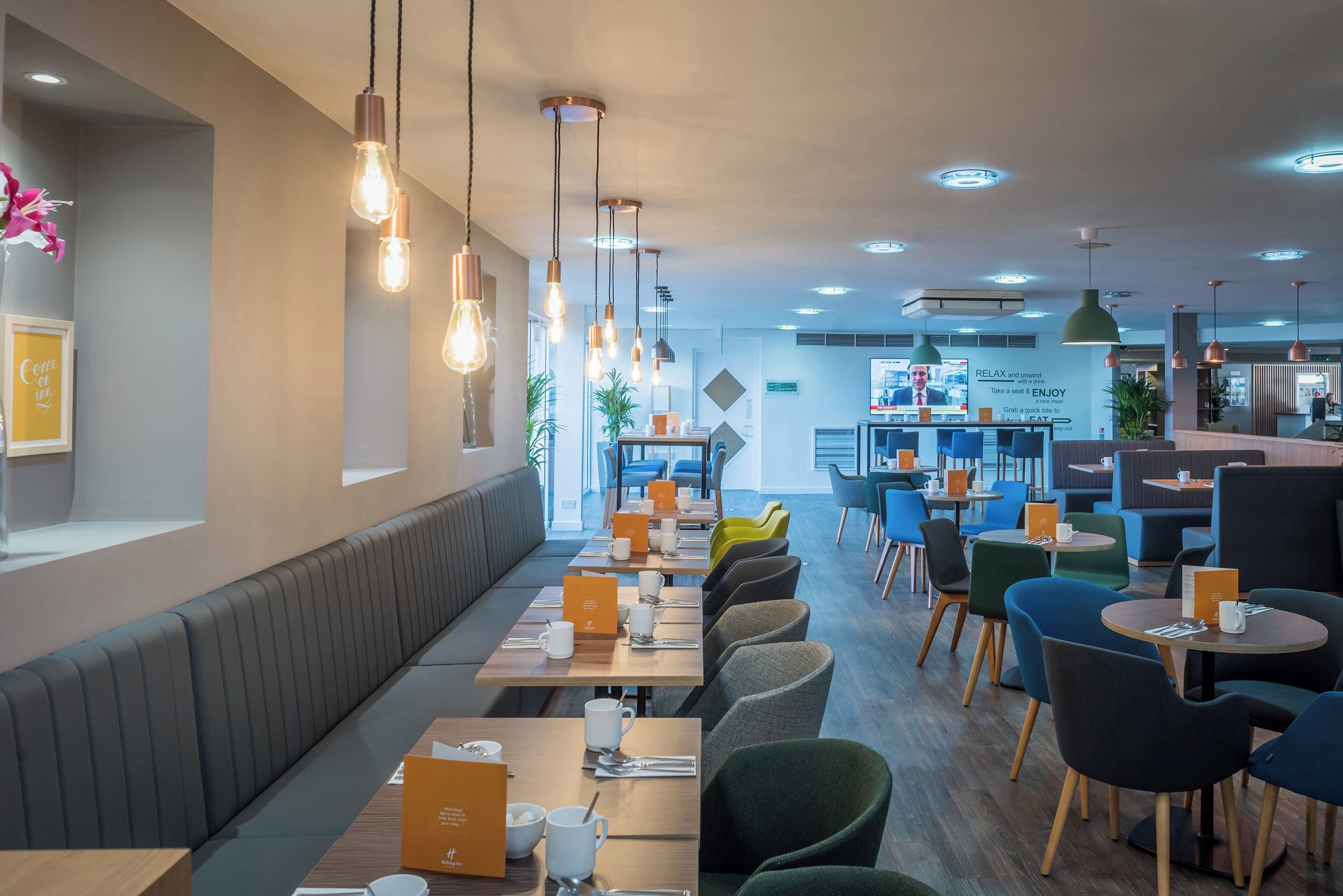 A modern restaurant with long communal tables, individual booths, and hanging pendant lights.