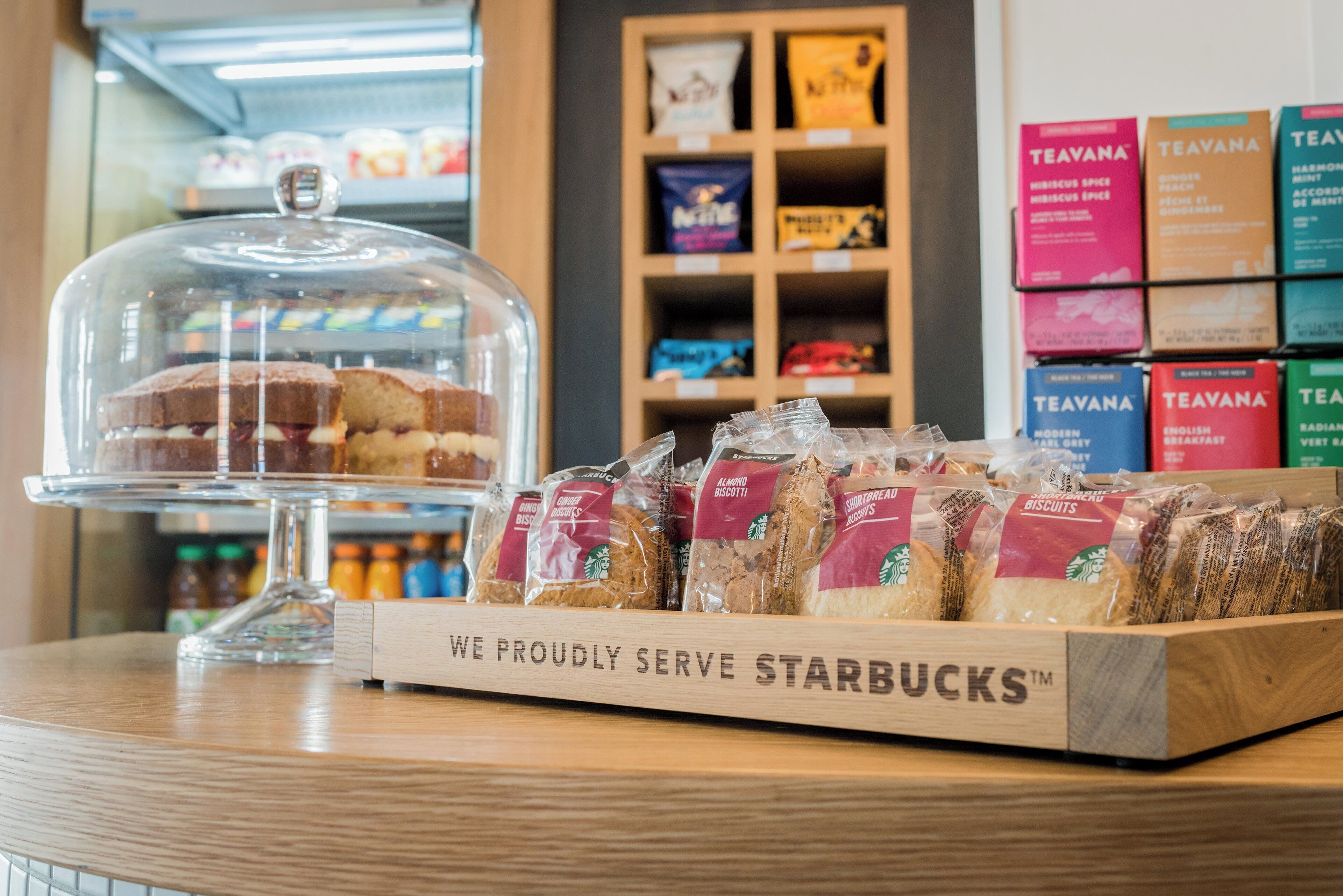 Une présentation de biscuits Starbucks et d’un gâteau sous un cloche de verre.