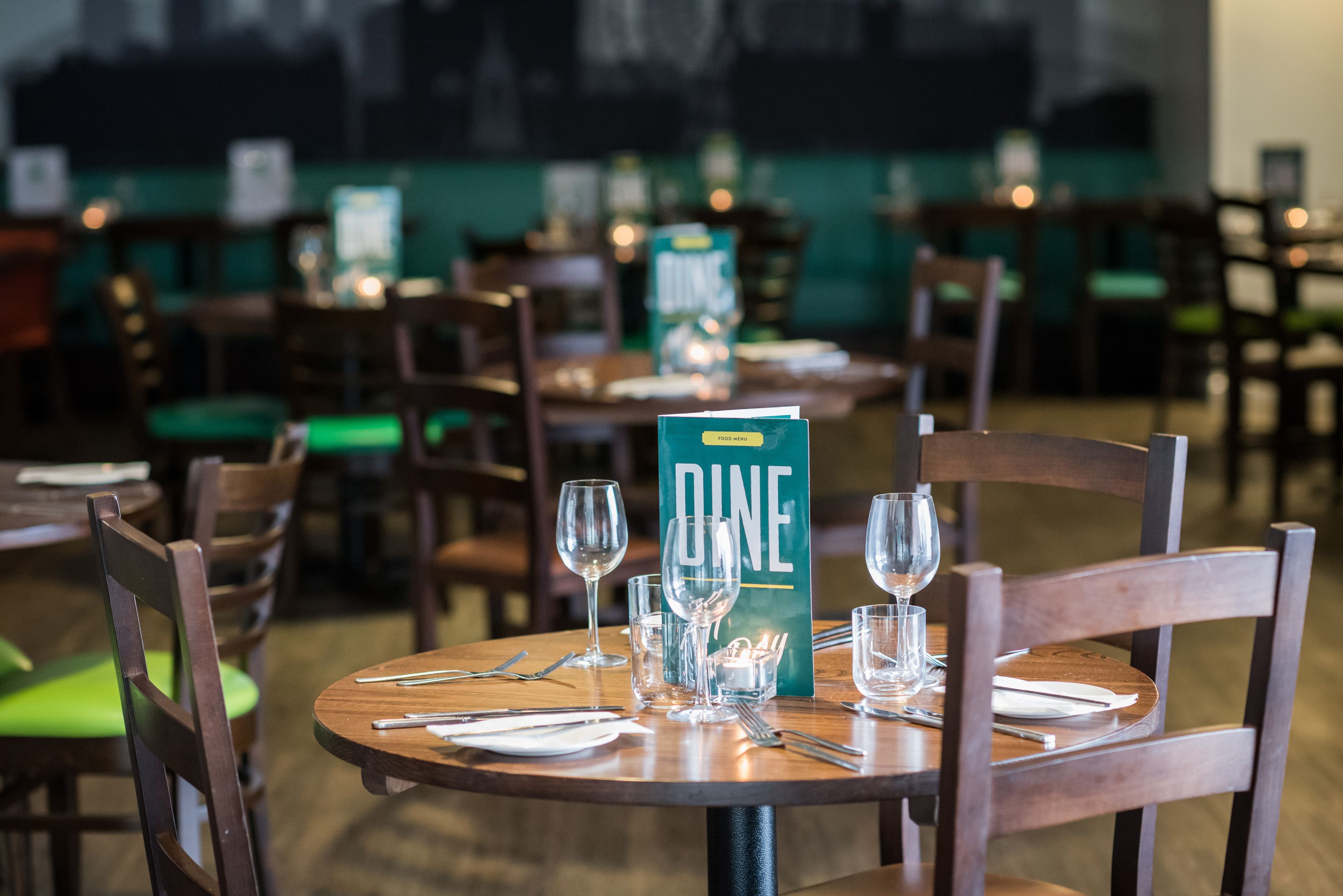 A restaurant setting with tables set for dining, chairs, and a menu stand.