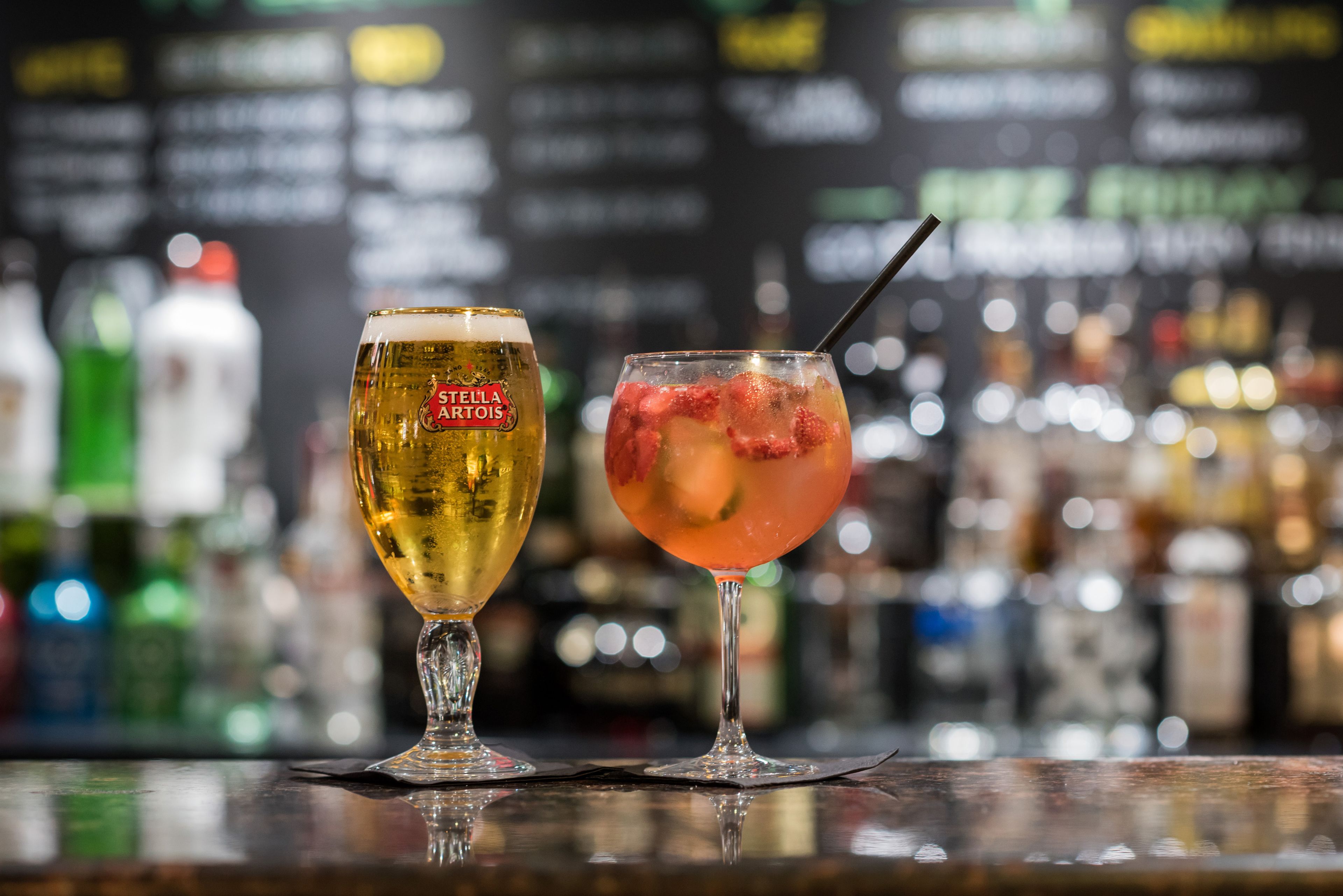 Deux verres de boissons sur le comptoir d’un bar, avec un arrière-plan flou composé de bouteilles.