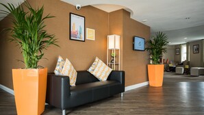 A modern lobby with a black leather sofa, orange planters, and framed pictures on the wall. - Holiday Inn Manchester West by IHG (Salford)