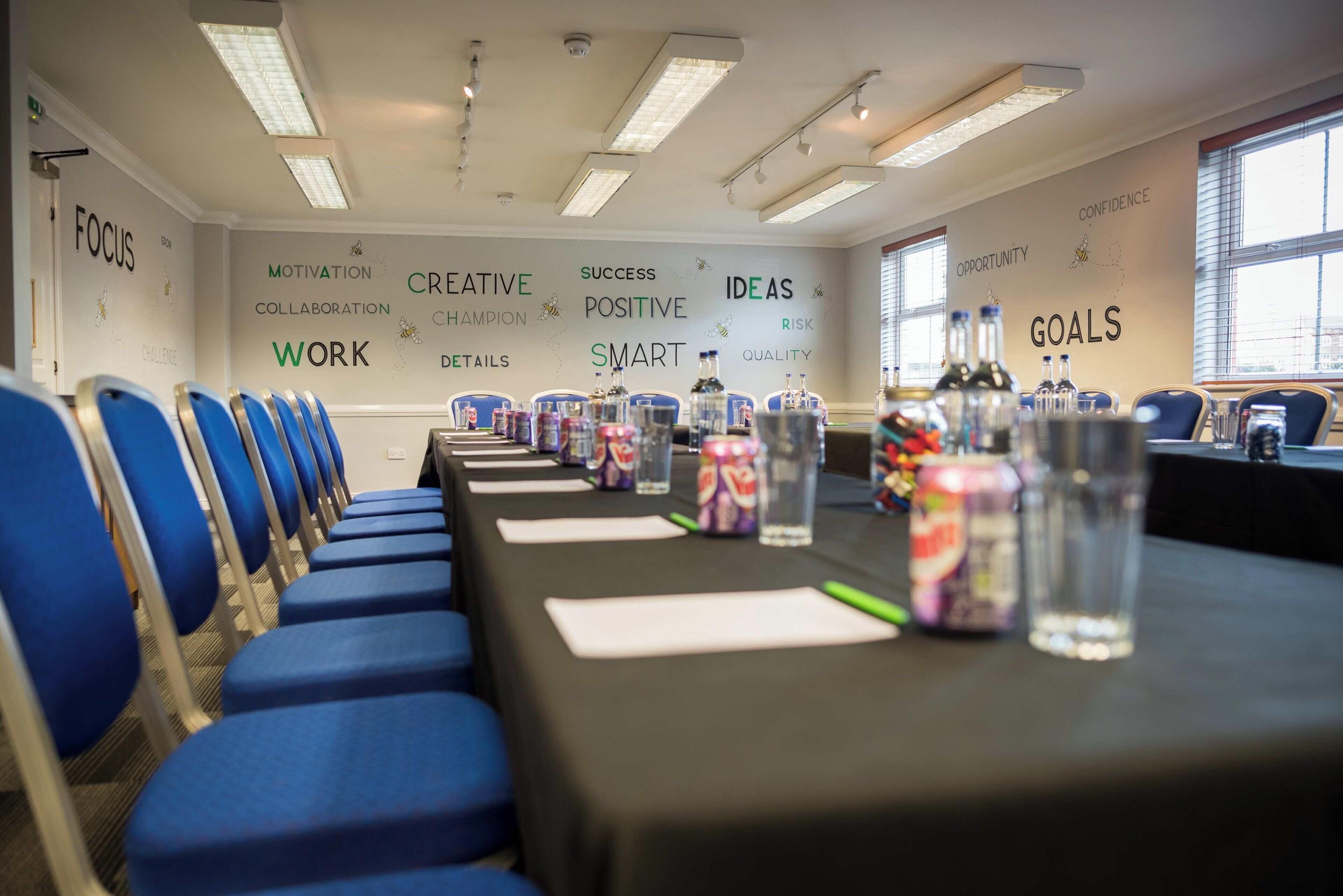 A conference room with rows of blue chairs, a long table with water bottles, and motivational words on the walls.