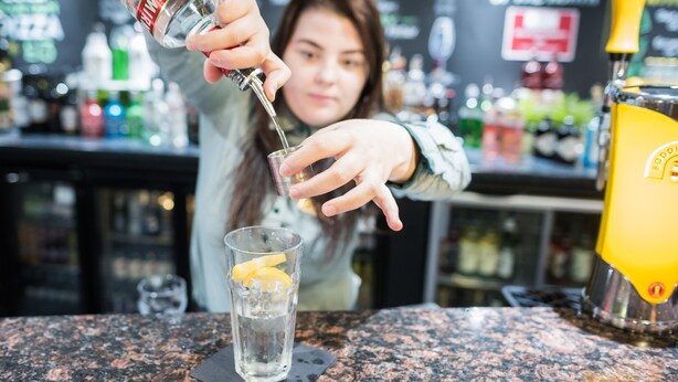 A bartender pouring a drink into a glass with a lemon slice. - Holiday Inn Manchester West by IHG (Salford)