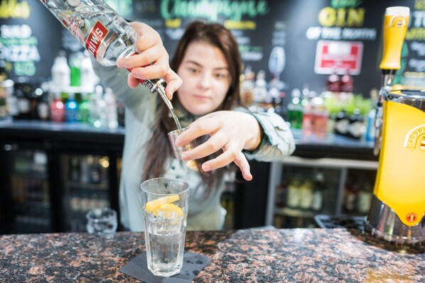 A bartender pouring a drink into a glass with a lemon slice. - Holiday Inn Manchester West by IHG (Salford)