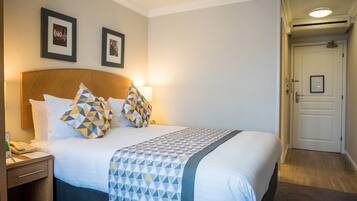 Une chambre d’hôtel avec un lit bien fait, une table de chevet avec une lampe et une porte donnant sur une autre pièce.
