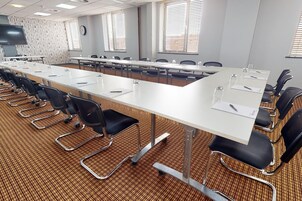 Un salón de conferencias con mesas largas, sillas negras y una alfombra estampada.