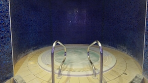 Ein runder Whirlpool mit Metallgeländern, umgeben von einem gefliesten Boden und Wänden mit blauem Mosaikmuster.
