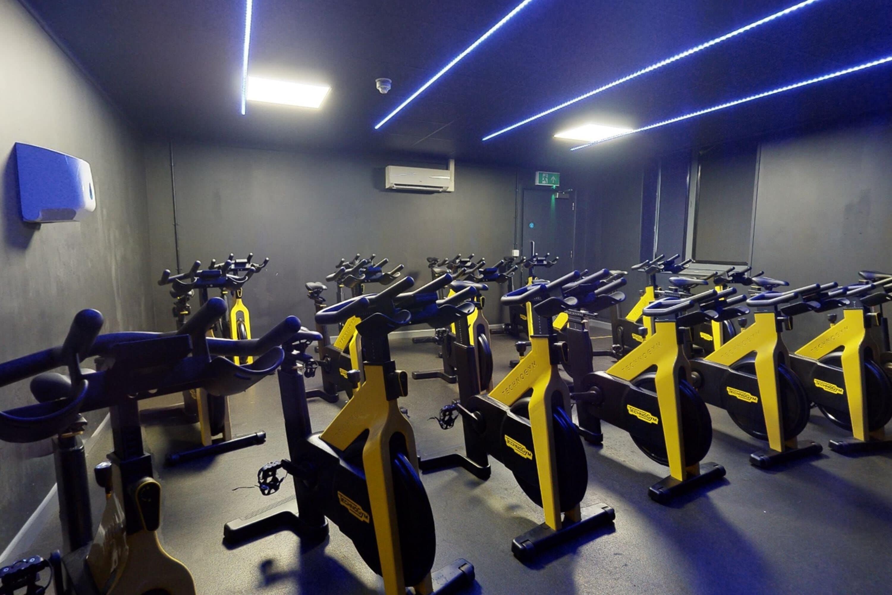 Une salle de sport équipée de plusieurs vélos d’exercice et de tapis de course disposés en rangées.