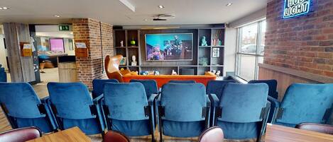 A modern bar area with blue chairs, a television, and a neon Bud Light sign.