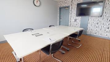 A conference room with a long table, four chairs, a clock, and a TV on the wall.