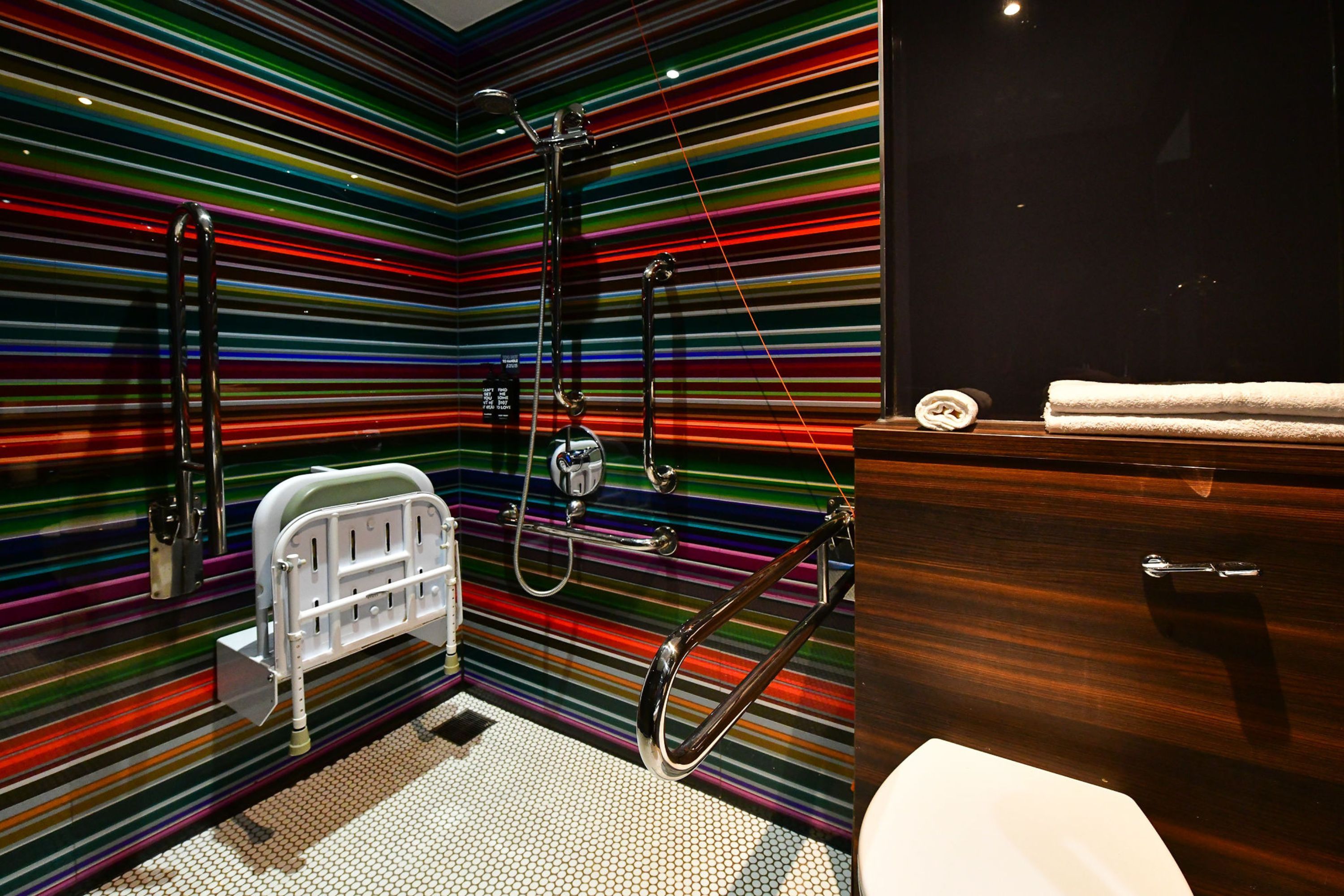 Une salle de bain au design moderne, dotée d’une douche avec un pommeau de douche amovible et de toilettes séparées par une paroi en verre.