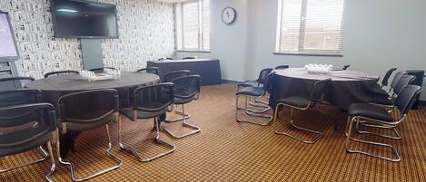 A conference room with a large flat-screen TV, multiple tables with chairs, and a patterned carpet.