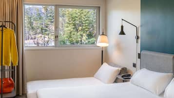 Habitación de hotel con cama, mesita de noche, lámpara y ventana con vista a árboles.