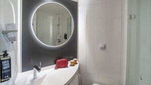 A bathroom with a large mirror, a white sink, a handheld showerhead, and a bottle of shampoo. - ibis Barcelona Aeropuerto Viladecans (Viladecans)