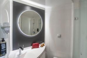 A bathroom with a large mirror, a white sink, a handheld showerhead, and a bottle of shampoo. - ibis Barcelona Aeropuerto Viladecans (Viladecans)
