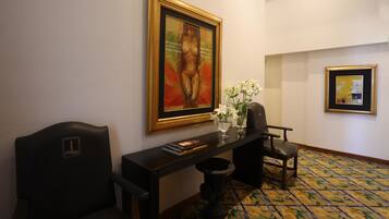 Un vestíbulo de hotel con un mostrador de recepción, dos sillones, un jarrón con flores y dos cuadros en la pared.