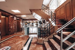 Un vestíbulo con suelo de mármol, una escalera central, un mostrador de recepción y una decoración floral.