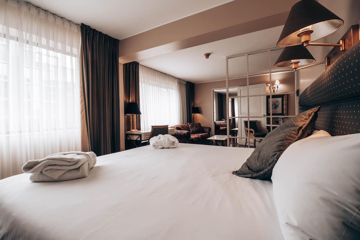 A hotel room with a large bed, a desk, a chair, and a mirror.