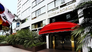A hotel entrance with a red awning, palm trees, and a sign reading "SUITES del BOSQUE". - Suites del Bosque Hotel (Lima)