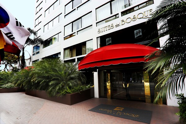 A hotel entrance with a red awning, palm trees, and a sign reading "SUITES del BOSQUE". - Suites del Bosque Hotel (Lima)