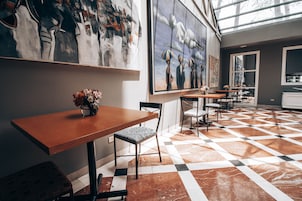 Un interior moderno con suelo a cuadros, mesas y sillas de madera, y grandes cuadros abstractos en las paredes.