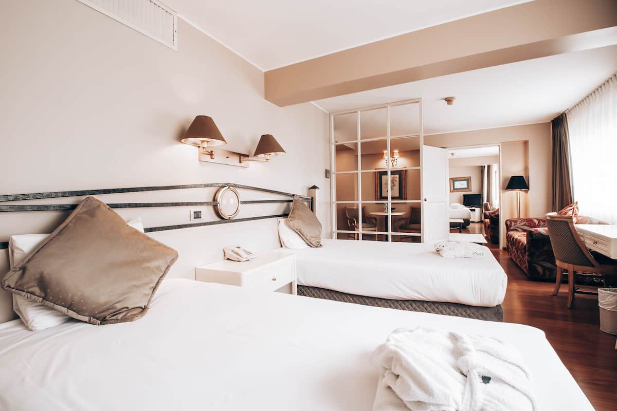 A hotel room with two beds, a desk, a chair, and a dining area.