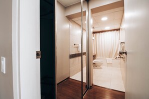 A modern bathroom with a glass shower door, a toilet, and a bathtub. - Suites del Bosque Hotel (Lima)